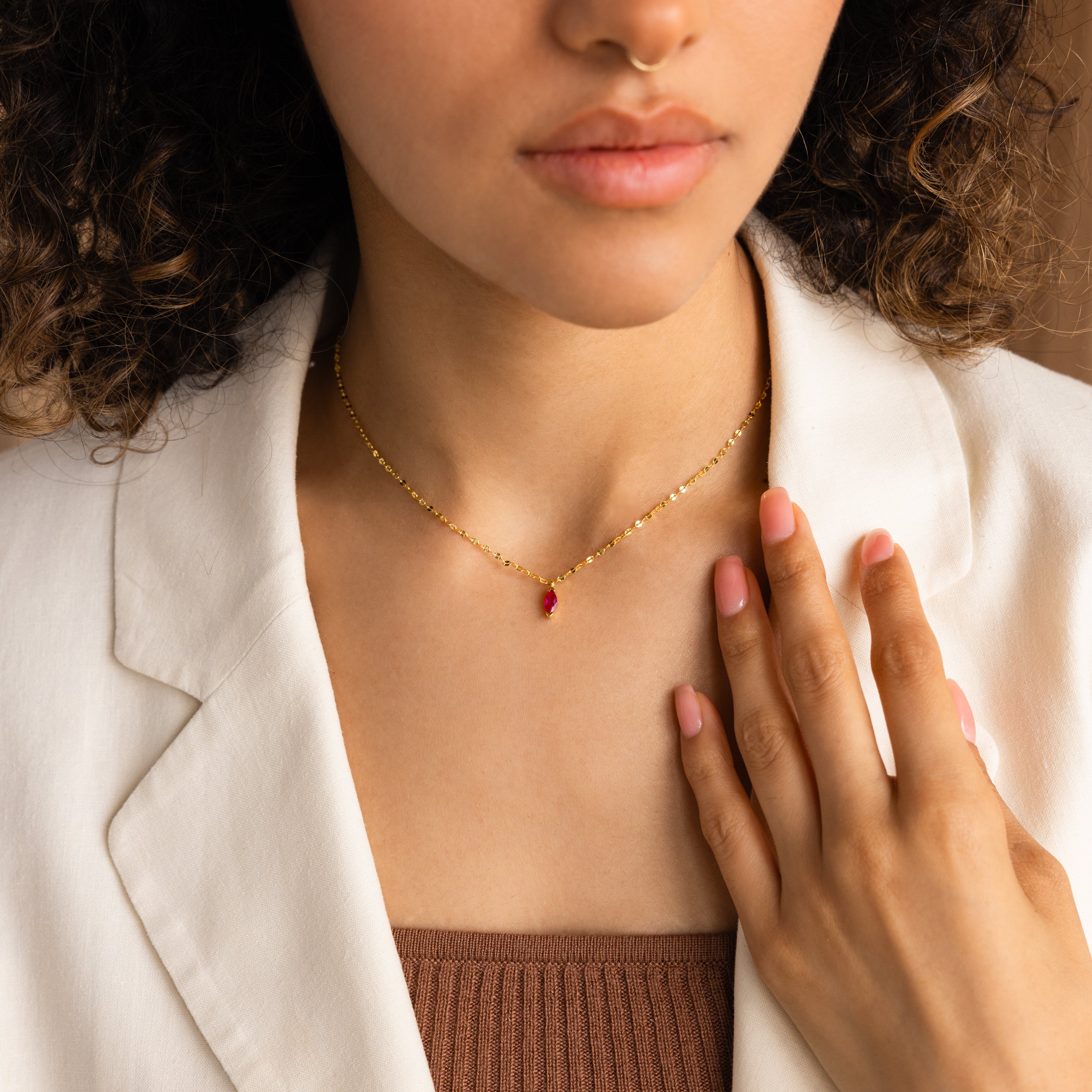 A woman in a white blazer and brown top wears the Custom Marquise Birthstone Necklace featuring a red marquise-cut pendant.