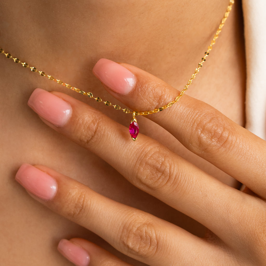 A hand with pink nails holds the Custom Marquise Birthstone Necklace, featuring a shimmering marquise-cut pendant.