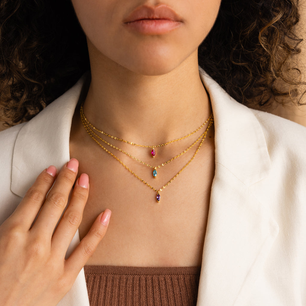 Woman wearing a white blazer and layered gold necklaces, including a colorful Custom Marquise Birthstone Necklace.