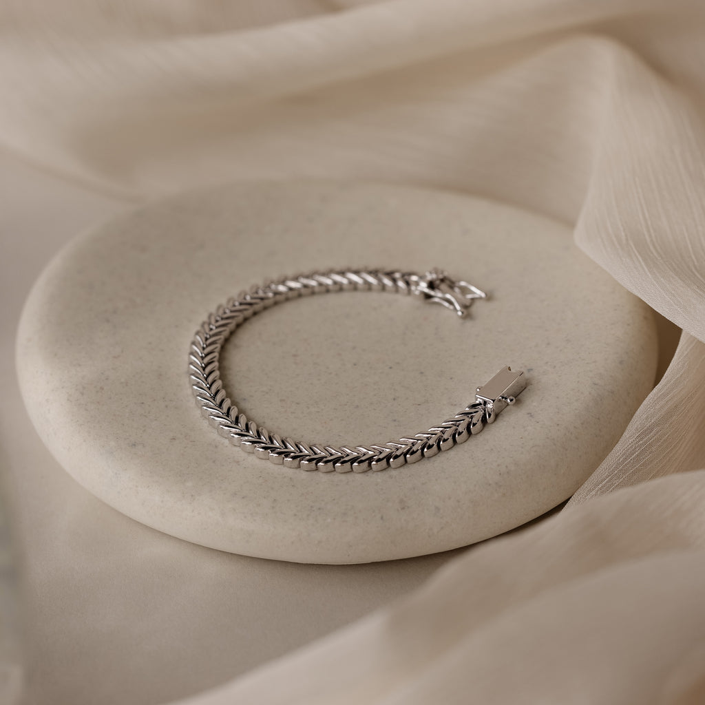 The V-Link Chain Tennis Bracelet, featuring sculptural silver links, is showcased on a round light stone with a soft beige fabric background.