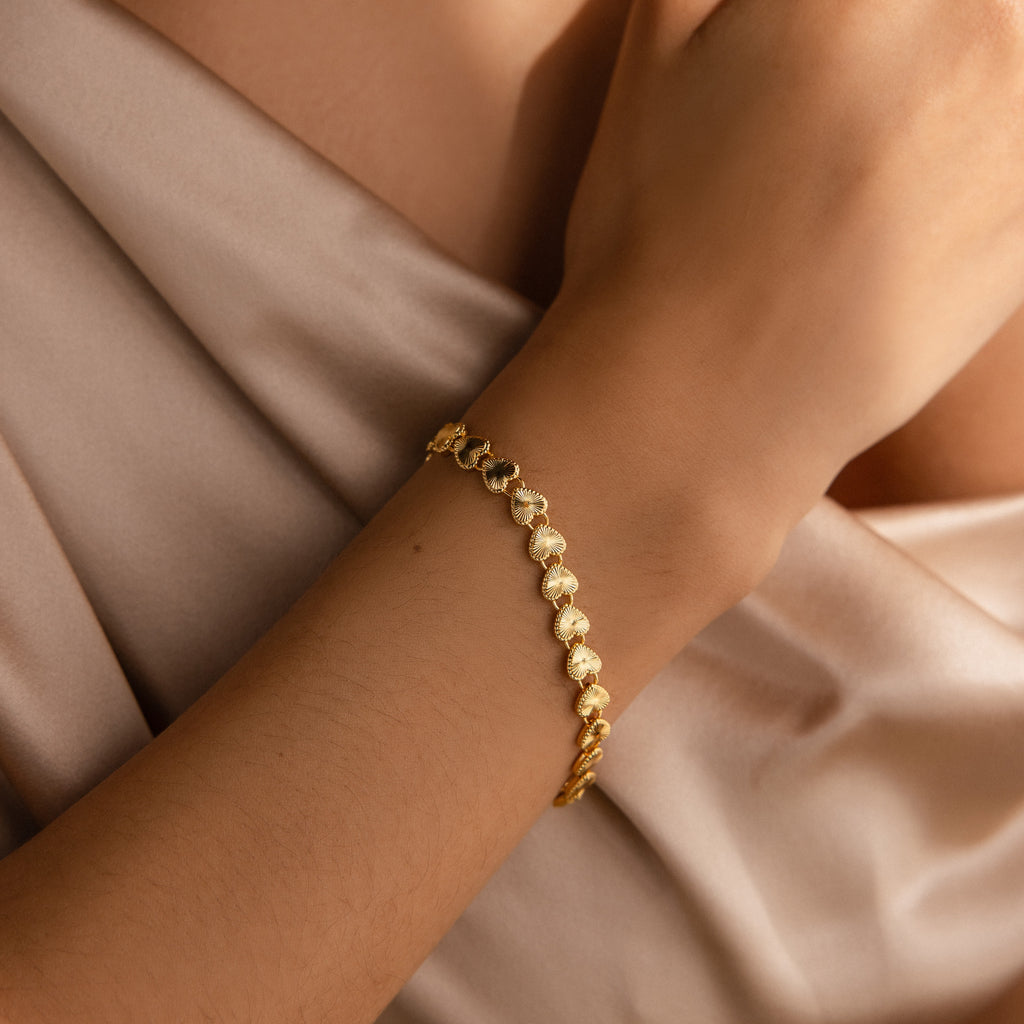 A model wearing the Ribbed Heart Link Bracelet on her wrist, styled with a soft champagne-colored dress.
