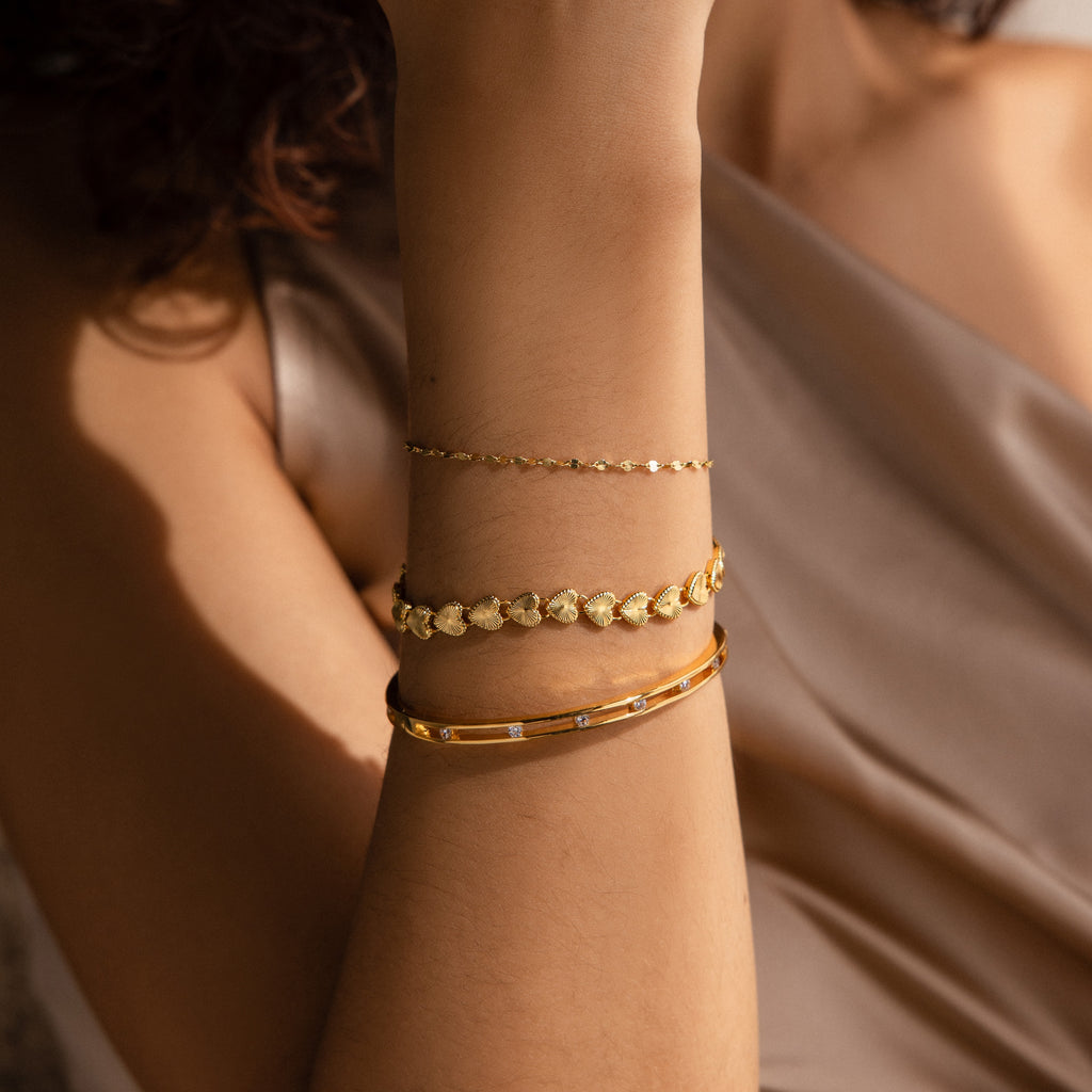 A close-up of a woman’s forearm adorned with three stacked bracelets, with the Ribbed Heart Link Bracelet in the center. 