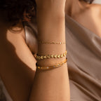 A close-up of a woman’s forearm adorned with three stacked bracelets, with the Ribbed Heart Link Bracelet in the center. 
