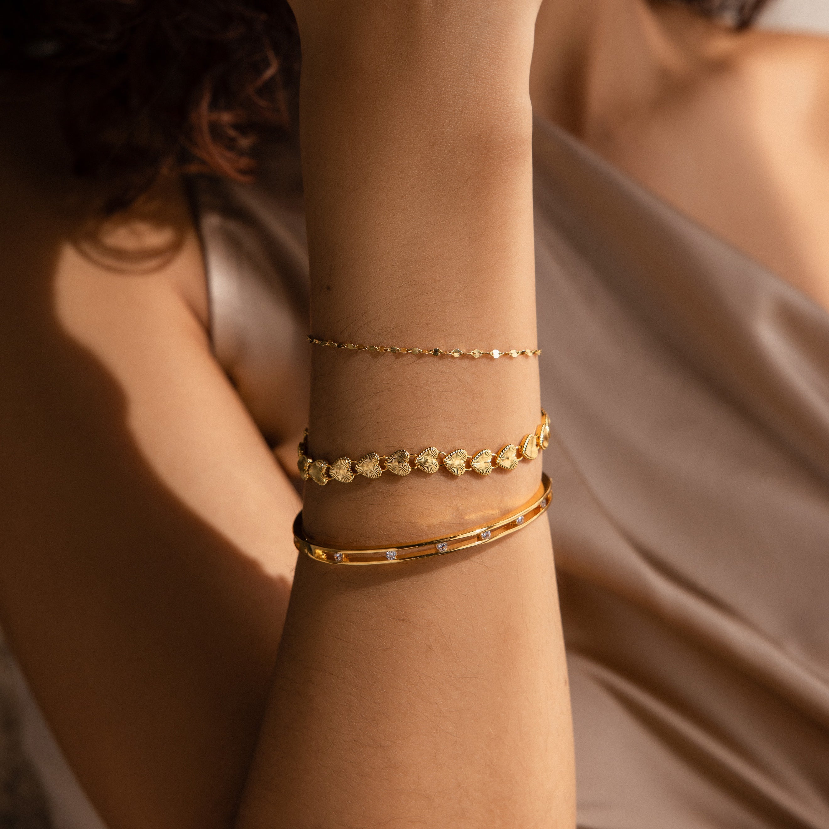 A close-up of a woman’s forearm adorned with three stacked bracelets, with the Ribbed Heart Link Bracelet in the center. 