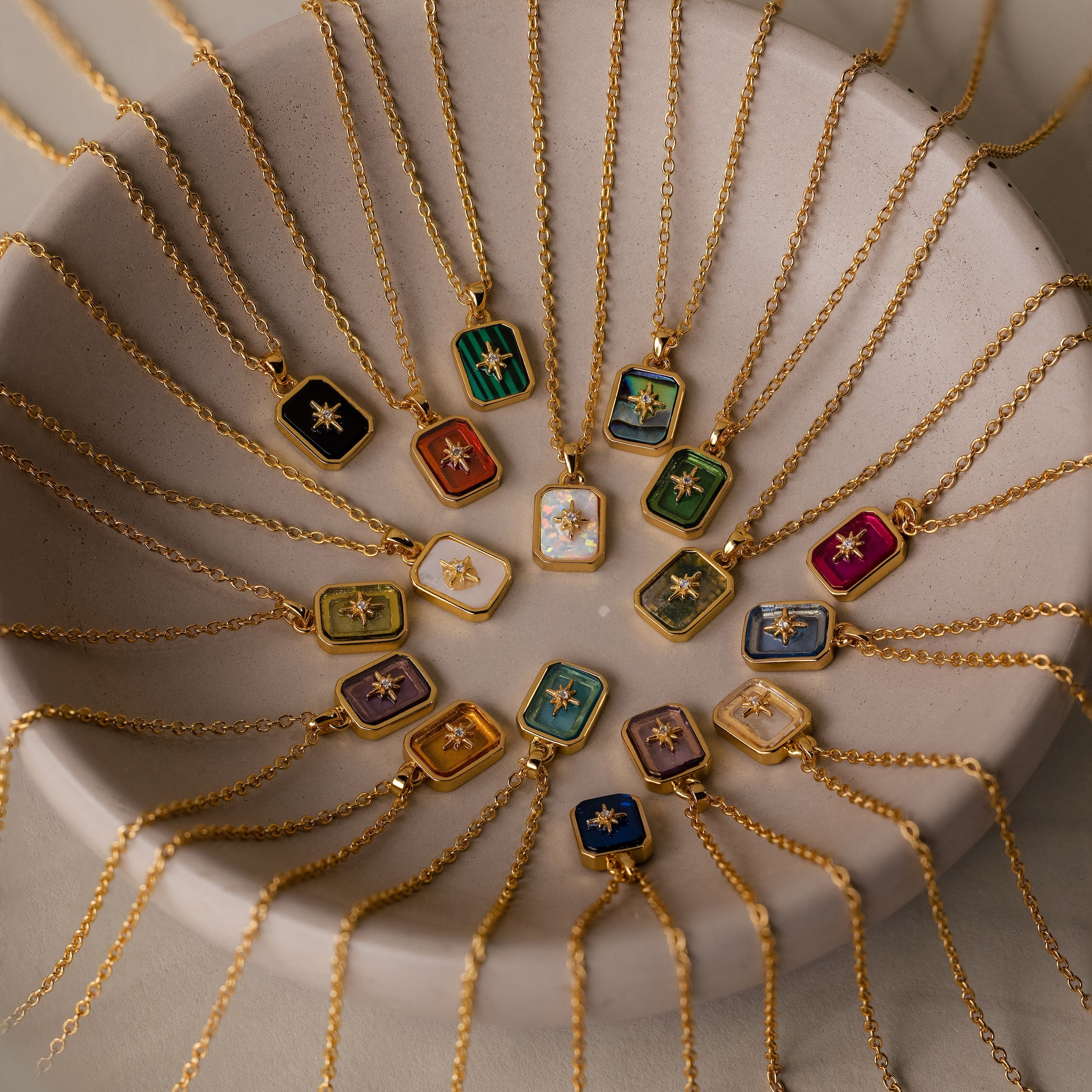 North Star Garnet Necklaces with colorful crystal pendants are arranged in a circle on a round beige dish.