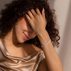 A woman gently smiles with her hand resting across her forehead, wearing the Ribbed Heart Link Bracelet in White Gold on her wrist. 