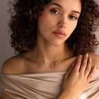 Woman with curly hair wearing an Ivy Diamond Station Necklace in 18K Gold and a nose ring, draped in beige off-shoulder fabric.