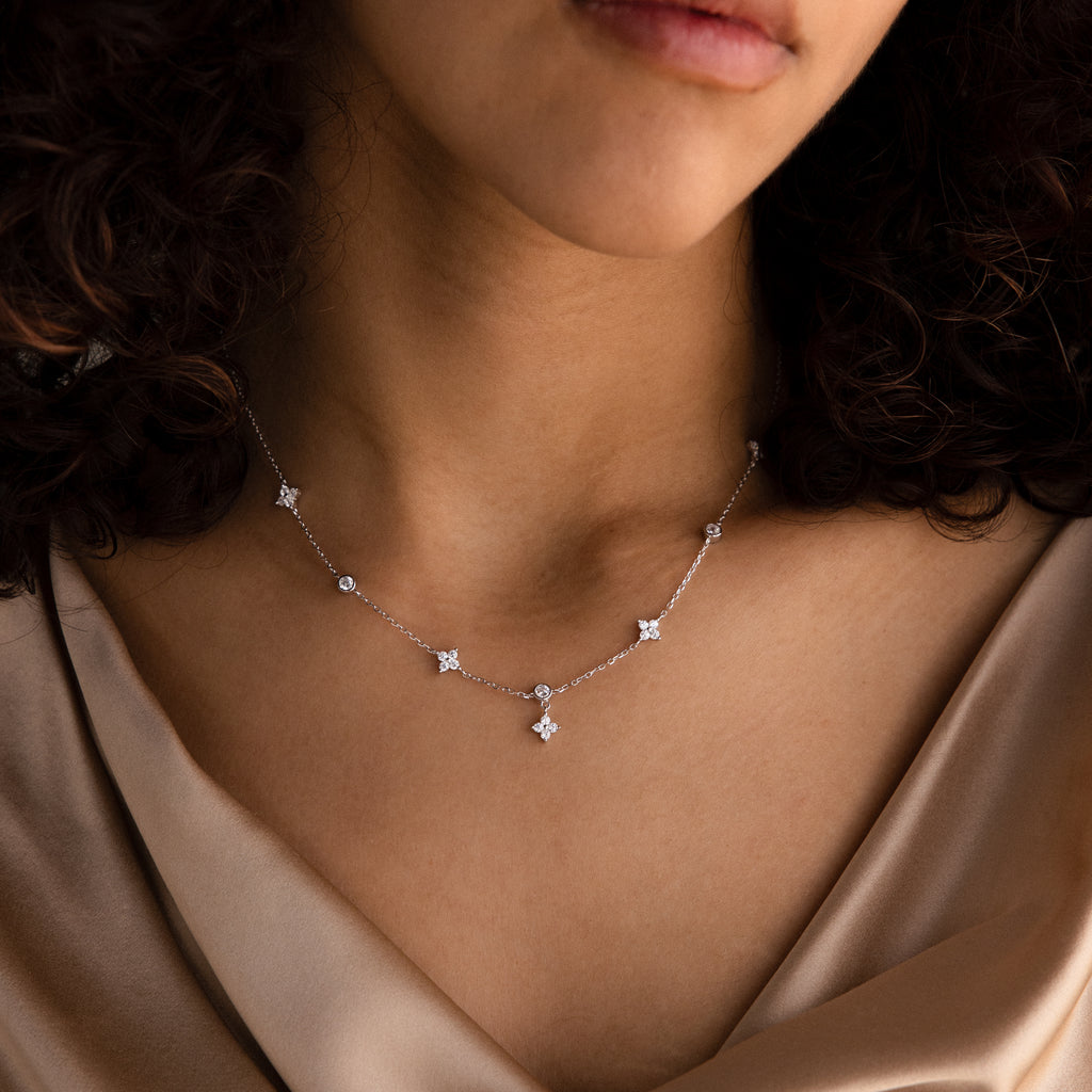 A woman wearing the Ivy Diamond Station Necklace in Silver, featuring small star-shaped pendants and diamond accents, paired with a silky beige top.