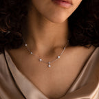 A woman wearing the Ivy Diamond Station Necklace in Silver, featuring small star-shaped pendants and diamond accents, paired with a silky beige top.