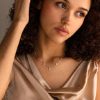 A woman with curly hair, wearing a satin top and a nose ring, gazes thoughtfully aside while showcasing the Ivy Diamond Station Necklace.
