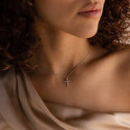 A woman with curly hair wears an off-shoulder beige top, her look completed by the Pave Cross Necklace for an elegant touch.