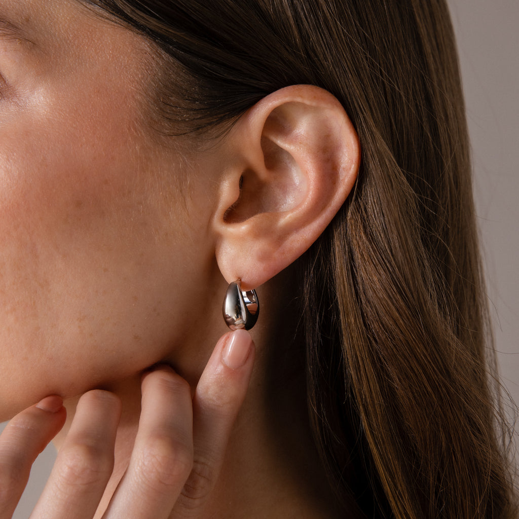 Close-up of a woman wearing Bold Teardrop Earrings in White Gold, gently touching her neck.