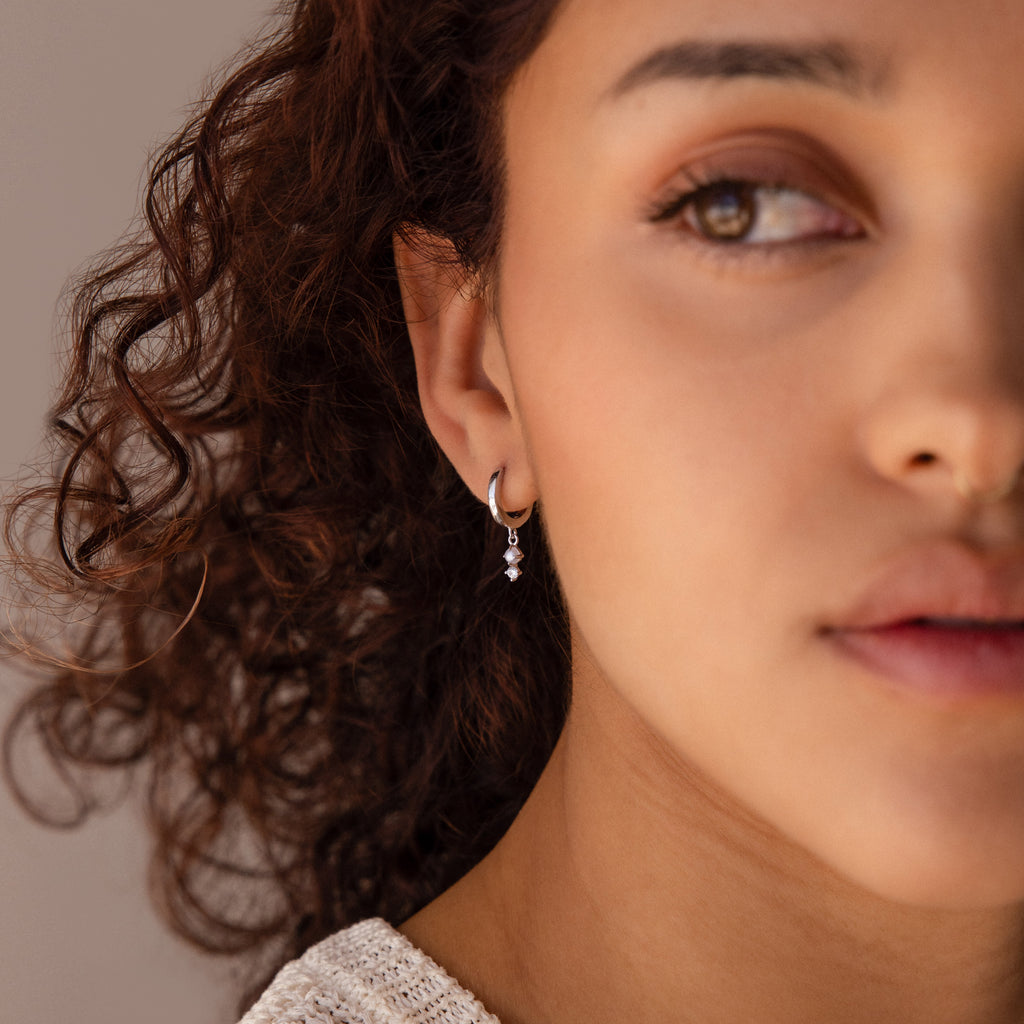 Woman with curly hair wearing elegant Dangling Pearl Diamond Huggies in Sterling Silver, shown in soft natural light, close-up on her face.
