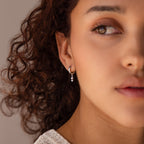 Woman with curly hair wearing elegant Dangling Pearl Diamond Huggies in Sterling Silver, shown in soft natural light, close-up on her face.