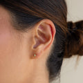 Close-up of a woman’s ear adorned with Ericka Diamond Studs; her hair is tied back in a bun, highlighting the delicate gold earrings.