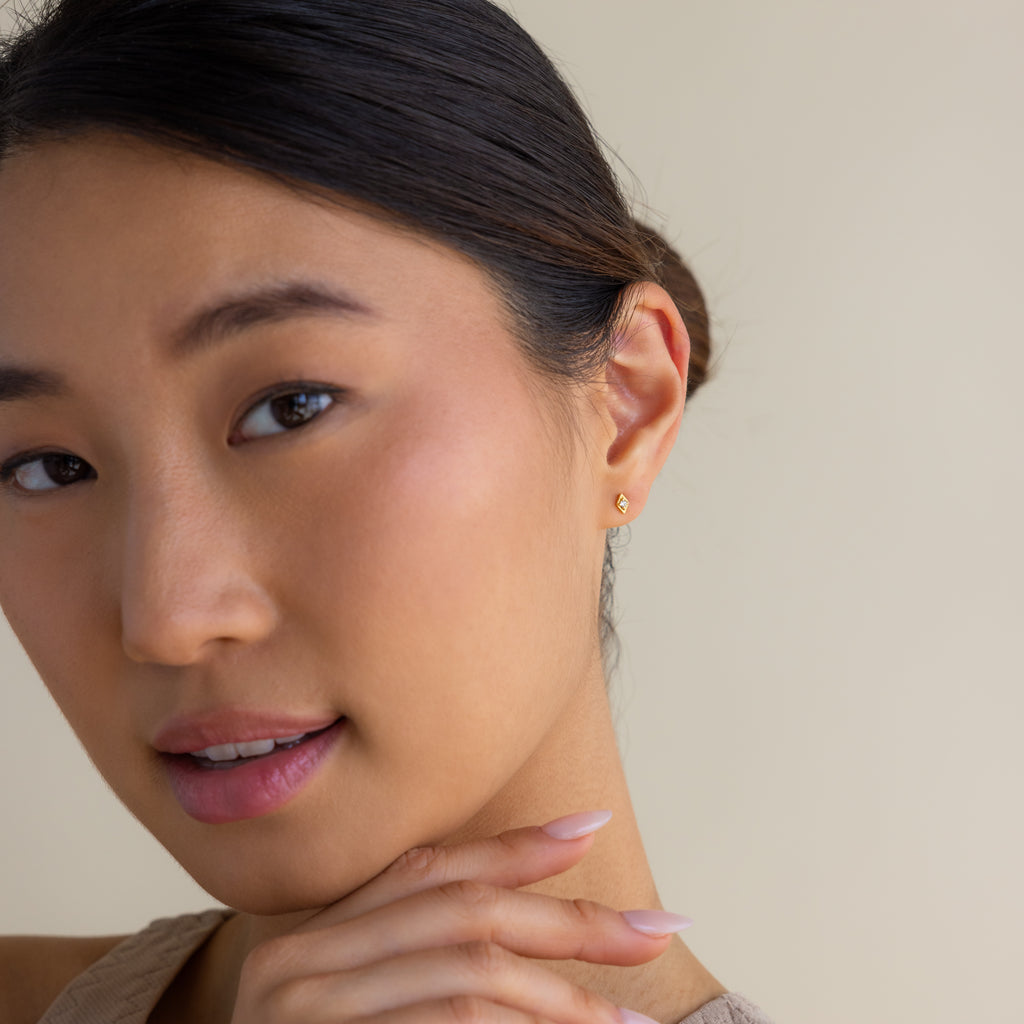 A woman with smooth skin and subtle makeup wears Ericka Diamond Studs, touching her chin against a neutral background.