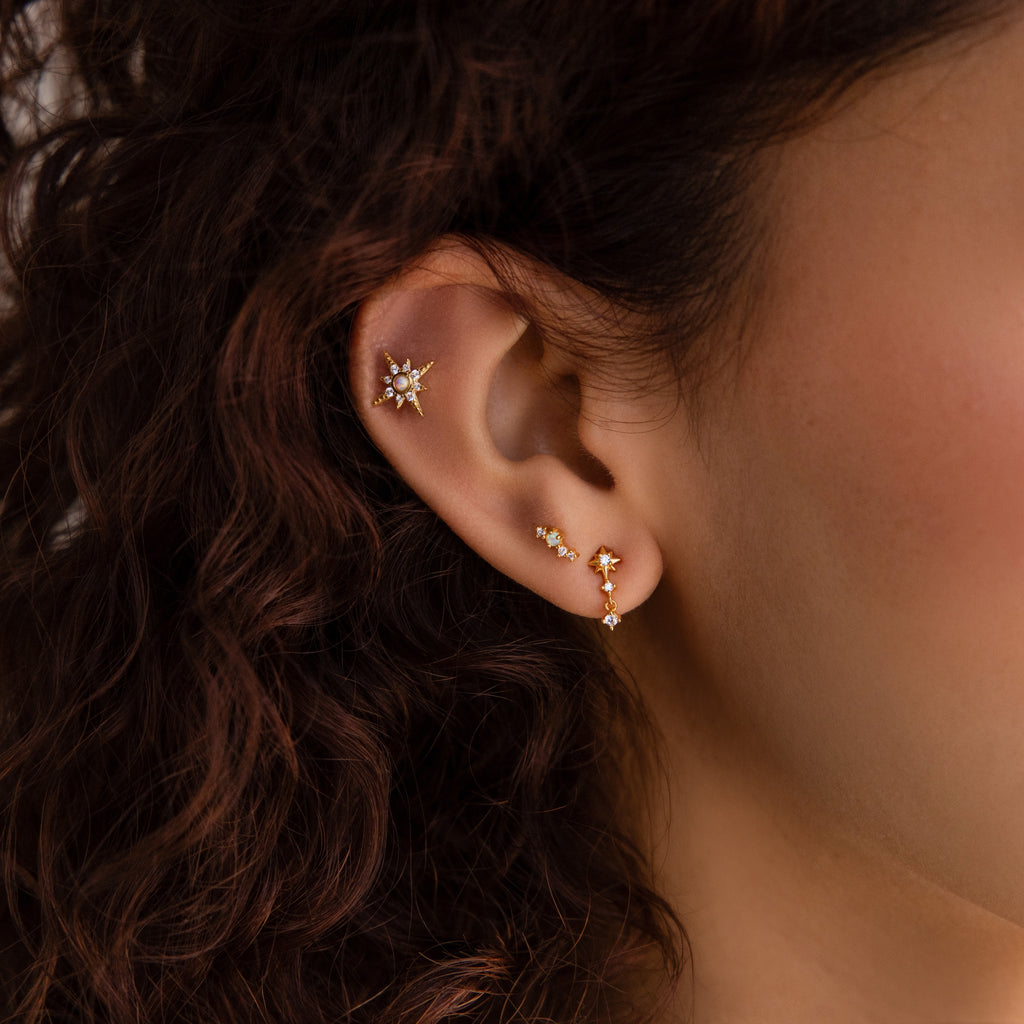 Close-up of a woman's ear with curly brown hair, showcasing the elegance of Diamond Starburst Drop Studs in 18K Gold, star-shaped diamond earrings.