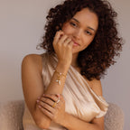 Woman with curly hair wears a satin top, gold jewelry, and the Hinged Circle Charm Bracelet, smiling softly at the camera.