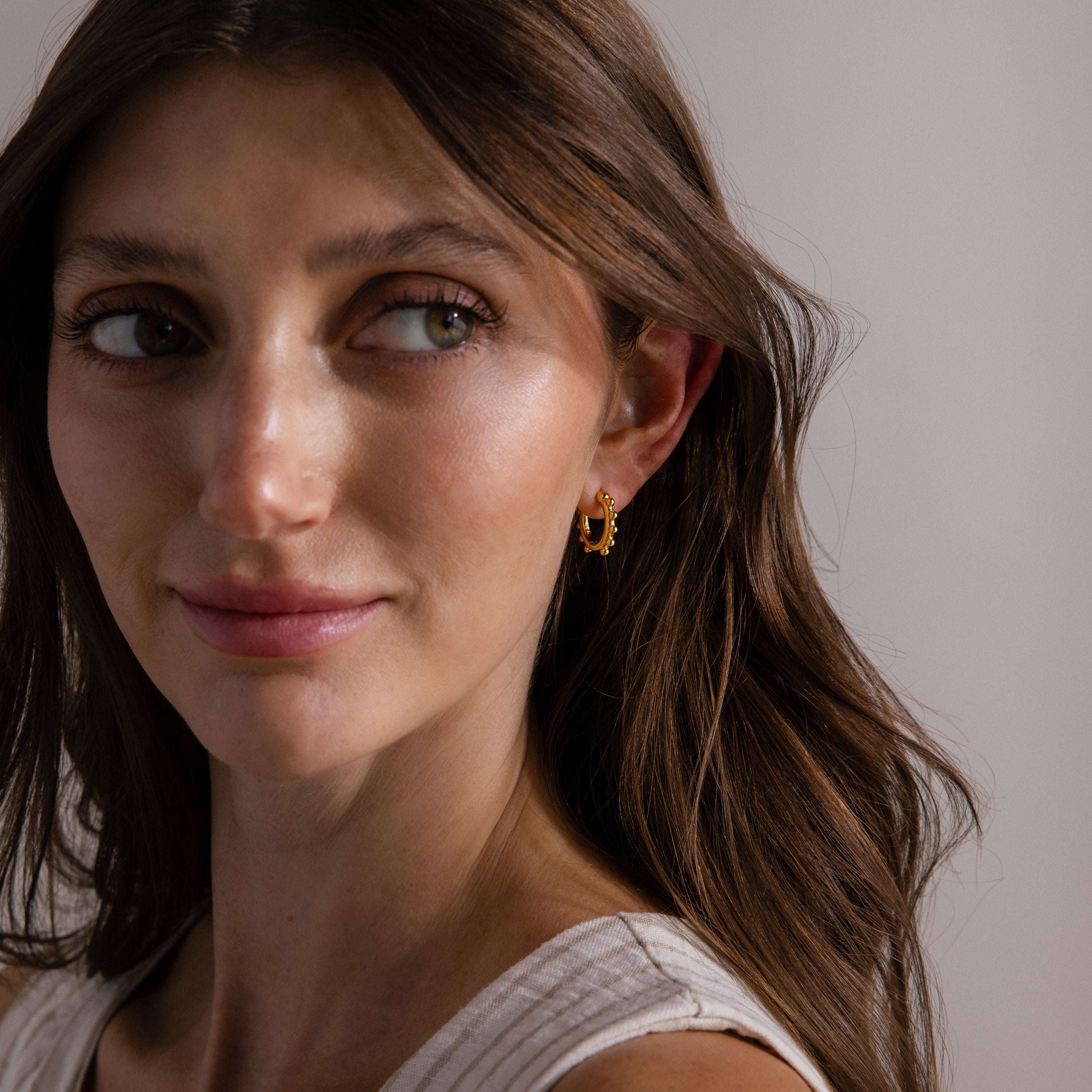 Woman with long brown hair wears Beaded Hoops in 18K Gold and a white top, looking slightly to the side.