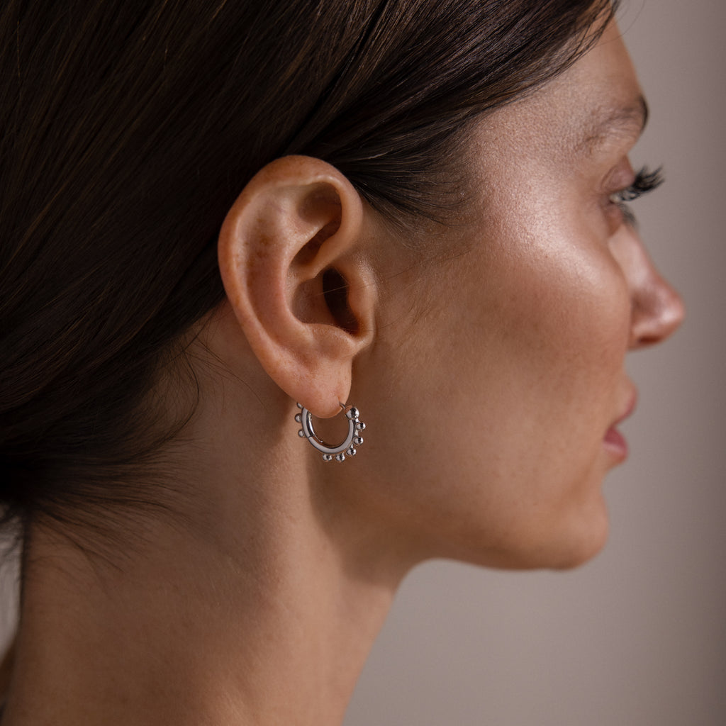A woman’s profile displays the Beaded Hoops, silver hoops accented with polished beads, showcasing their elegant style on her ear.