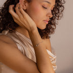 A woman with curly hair sits in sunlight, touching her face and wearing the Hinged Circle Charm Bracelet in Sterling Silver.