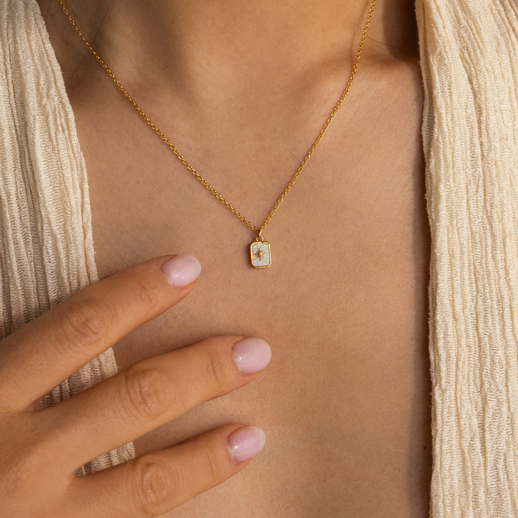 A person wearing the North Star Gemstone Necklace in 18K Gold touches their chest with manicured, light pink nails.