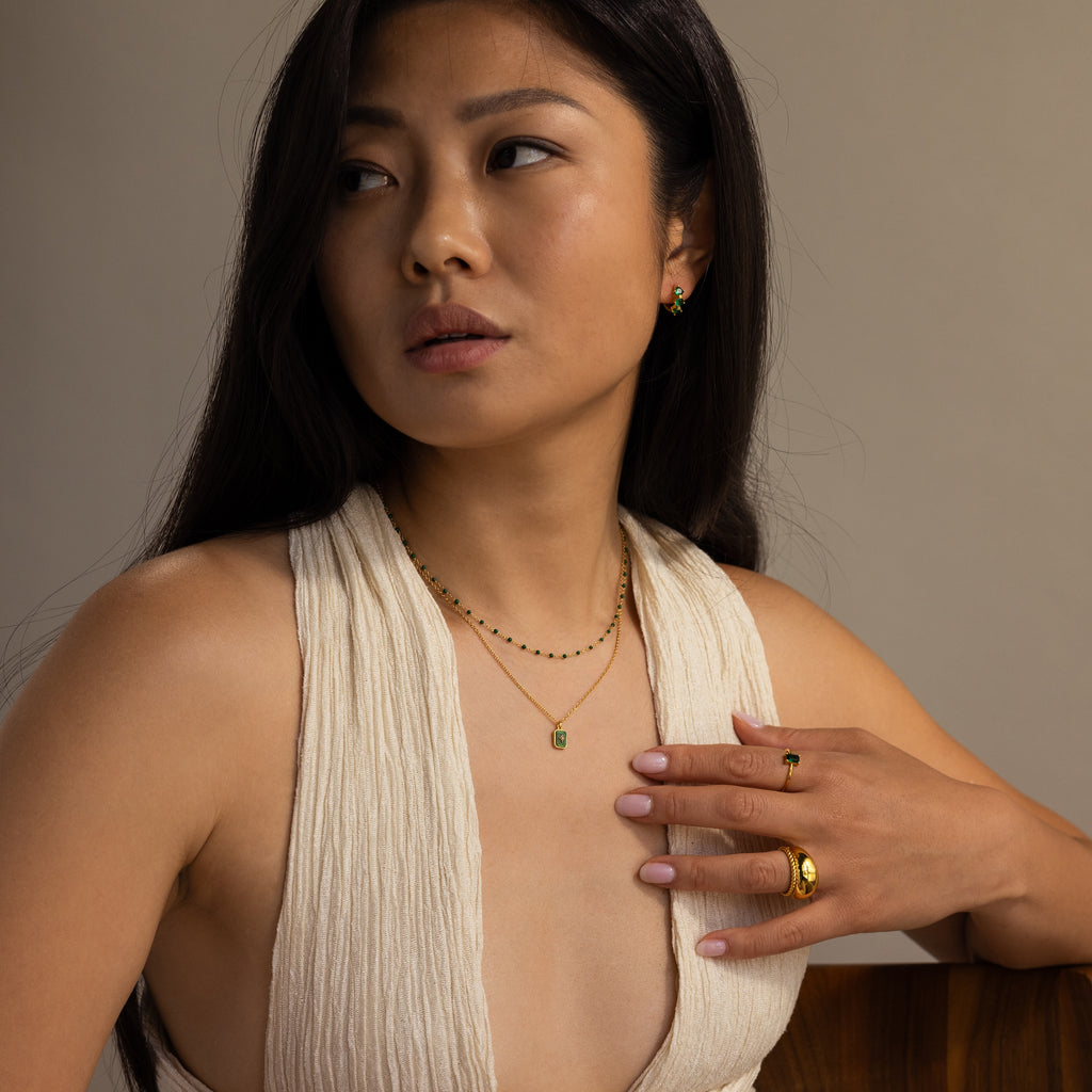 Woman in a cream sleeveless top wears gold jewelry and the North Star Gemstone Necklace in 18K Gold, gazing to the side with a neutral expression.