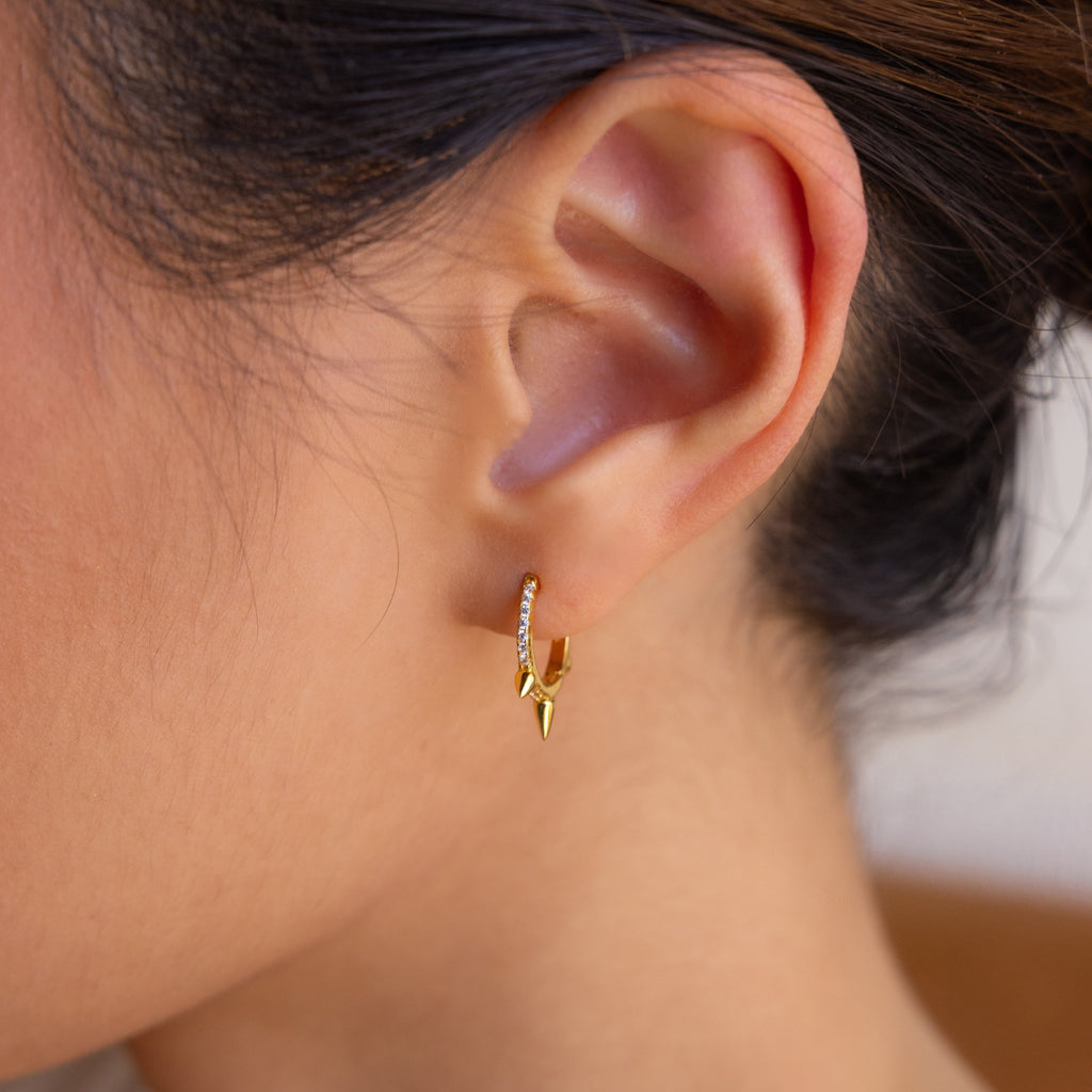 Close-up of a woman's ear wearing Pave Triple Spike Huggies—a minimalist gold hoop earring with delicate crystal accents.