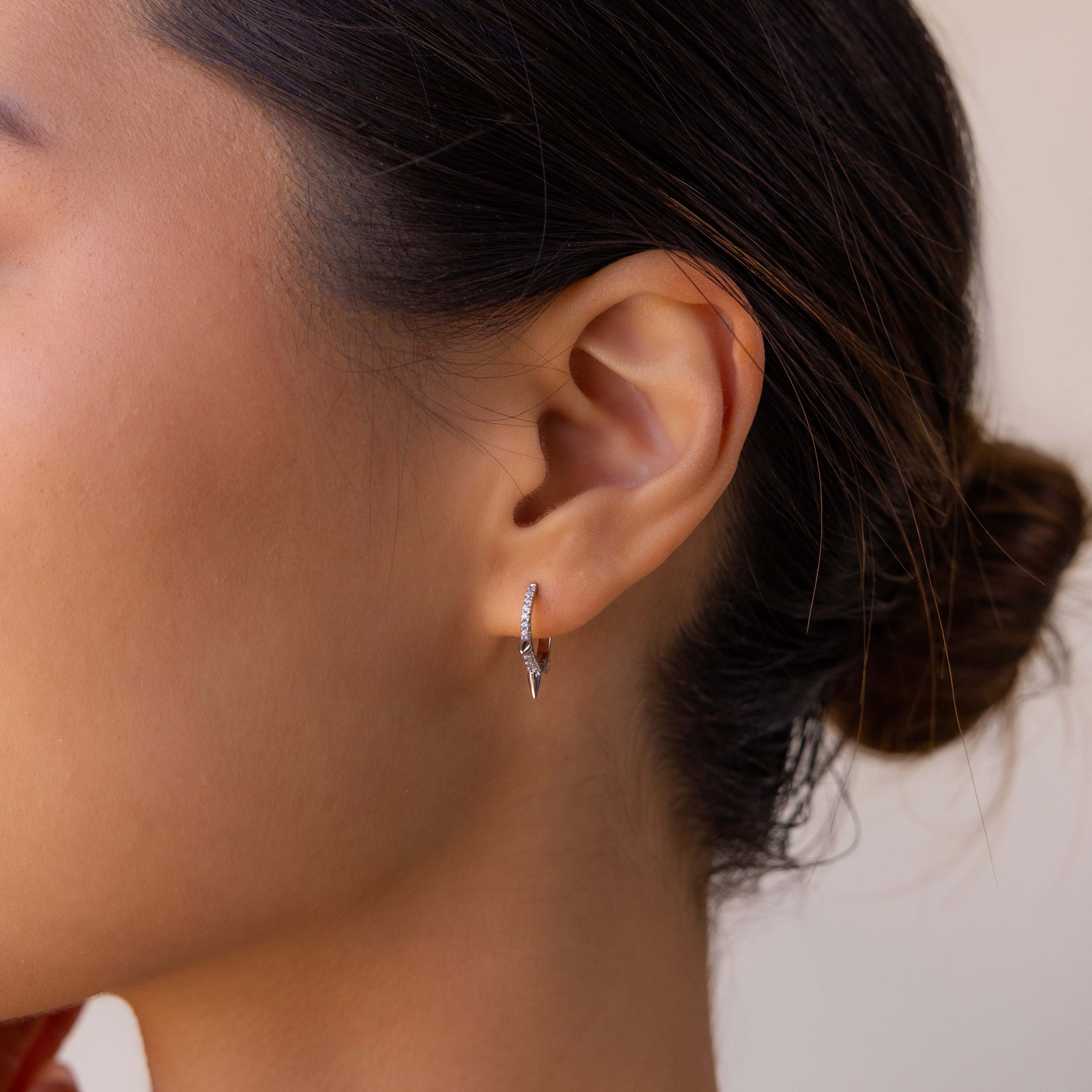 Close-up of a woman's ear wearing minimalist jewelry—Pave Triple Spike Huggies—with her dark hair tied in a bun.