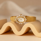 The Pave Heart Timepiece, adorned with heart-shaped gemstones and diamond accents, rests on a wavy cream surface against a neutral backdrop—adding a romantic touch to any look.