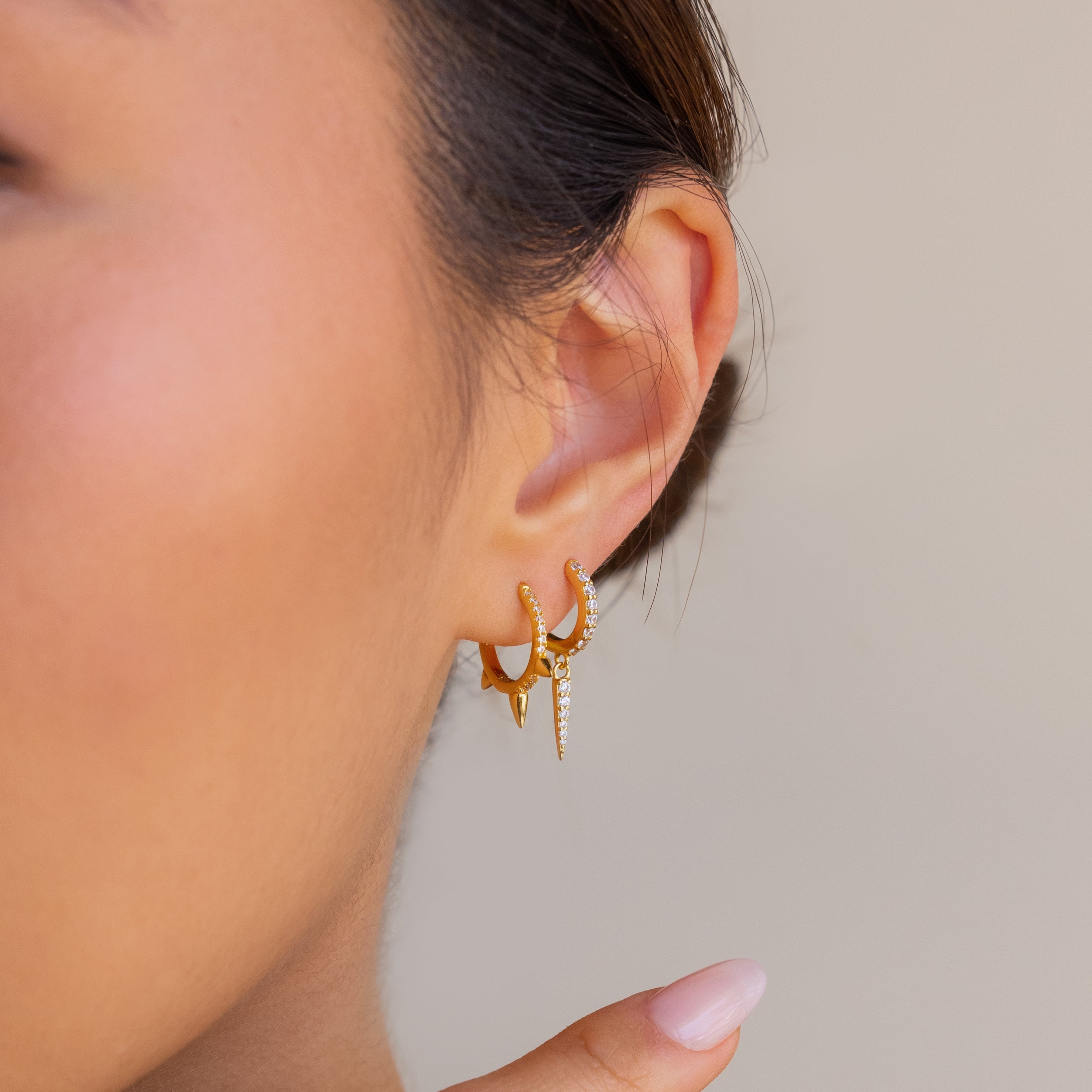 Close-up of a woman's ear wearing minimalist Pave Triple Spike Huggies—these earrings feature small rhinestones and spike-shaped pendants.