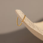 The Diamond Half Chain Ring, a delicate gold piece with sparkling diamonds, is styled with dainty jewelry and set on the edge of a textured beige surface.