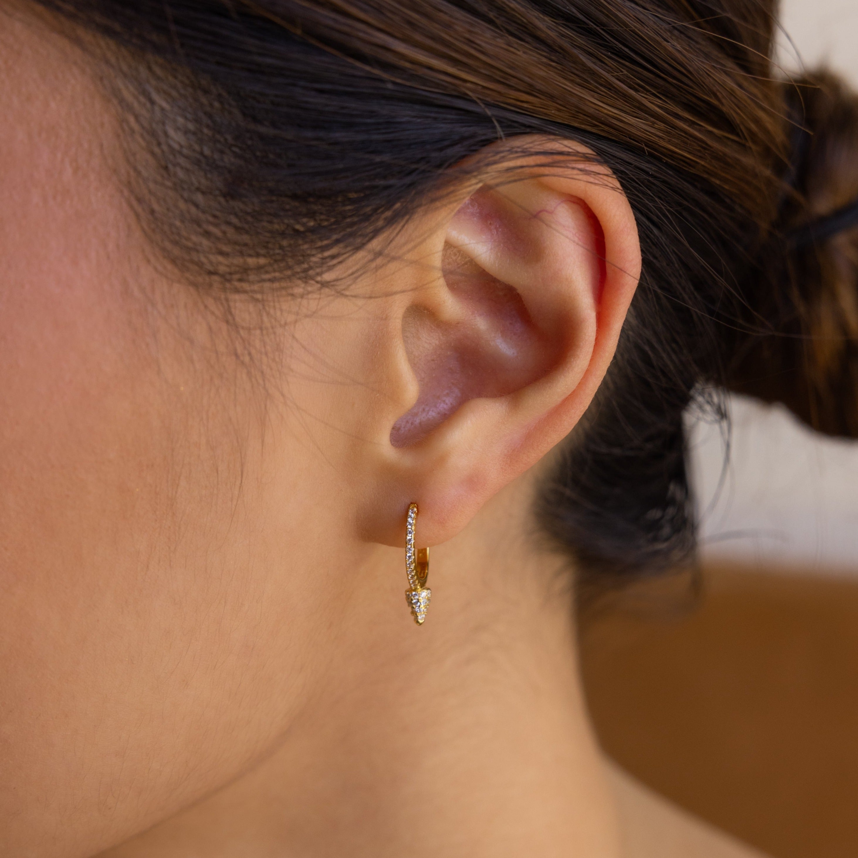 Close-up of a woman's ear wearing Pave Spike Huggies, small gold earrings with a row of dazzling pave-set gems in an edgy cone-shaped design.