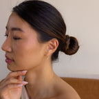 A woman with a low bun wears Pave Spike Huggies, the edgy cone design and sparkling pavé detail adding a modern touch as she poses thoughtfully with her hand near her chin.