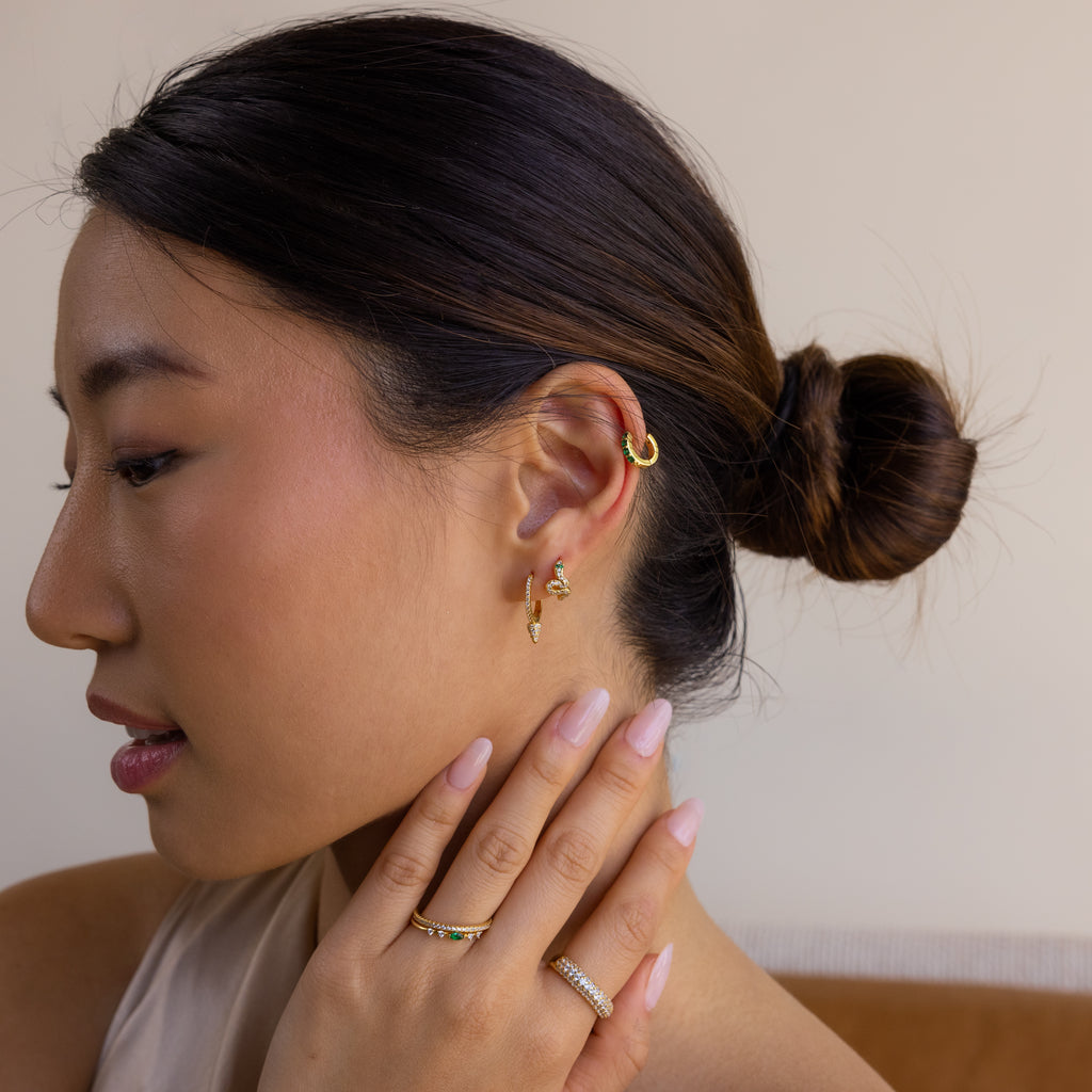 Woman with a low bun wearing Pave Spike Huggies and rings, touches her neck with manicured nails, creating an edgy cone-inspired look.