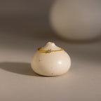 The Aquamarine Half Chain Ring, a delicate gold piece featuring a blue gemstone, rests gracefully on a small round off-white ceramic vase—a timeless, dainty jewelry accessory.