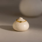 The Peridot Half Chain Ring is a delicate gold ring with a small peridot stone, shown on a smooth, round white ceramic holder—ideal for those who love dainty jewelry.