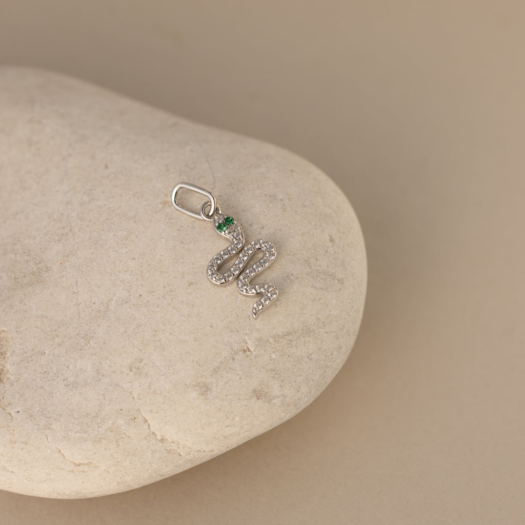 A silver diamond snake charm. The design is a twisting snake with diamond gemstones encased on its body and emerald gemstones for its eyes