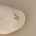 A silver diamond snake charm. The design is a twisting snake with diamond gemstones encased on its body and emerald gemstones for its eyes