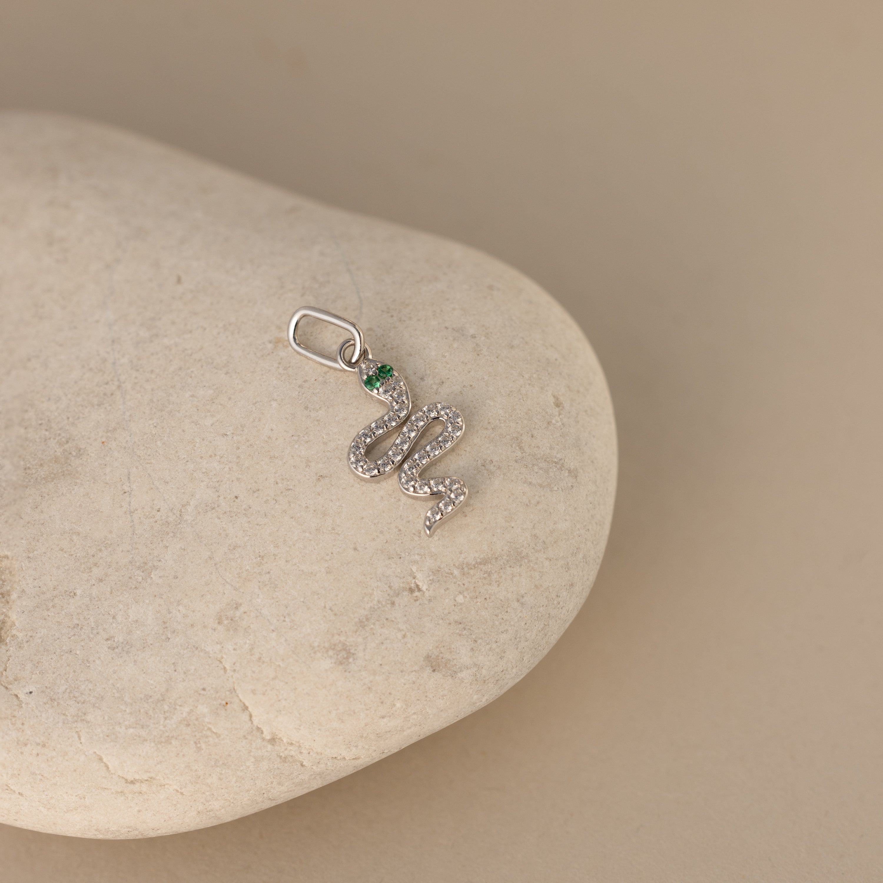A silver diamond snake charm. The design is a twisting snake with diamond gemstones encased on its body and emerald gemstones for its eyes