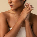 A woman with nude nails and minimal jewelry—a gold necklace, the Triple Snake Chain Bracelet in 18K Gold, and a ring—stands against a beige background.