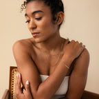 A woman in a white top styles her look with gold jewelry, featuring the Triple Snake Chain Bracelet for a layered effect, as she looks down with one arm crossed over her chest.