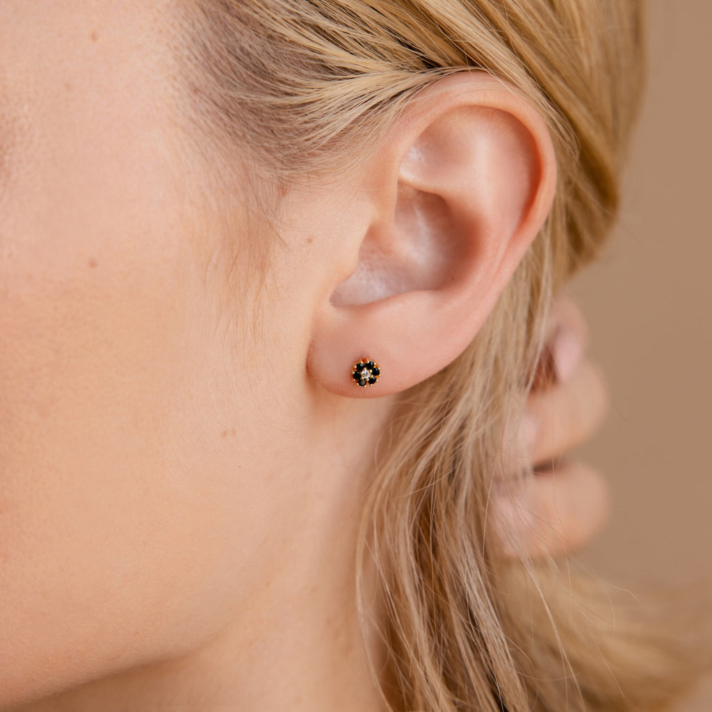 Close-up of a womans ear wearing Onyx Flower Studs, showcasing delicate black and gold flower-shaped details.