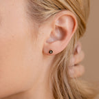 Close-up of a womans ear wearing Onyx Flower Studs, showcasing delicate black and gold flower-shaped details.