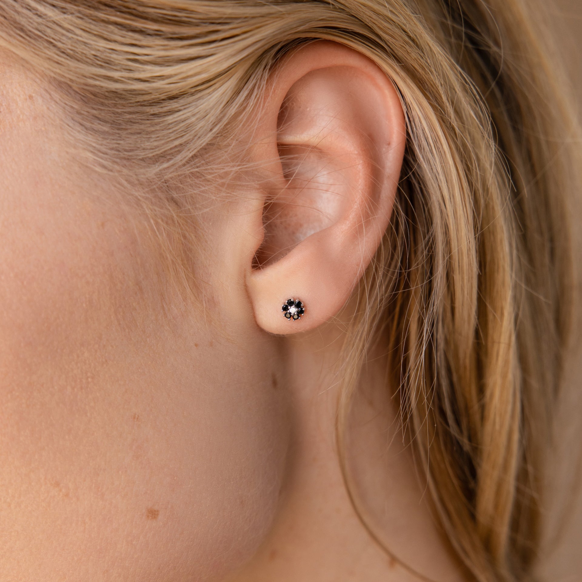 Close-up of a womans ear wearing Onyx Flower Studs in Silver, featuring small black and white onyx flowers with a delicate diamond center.