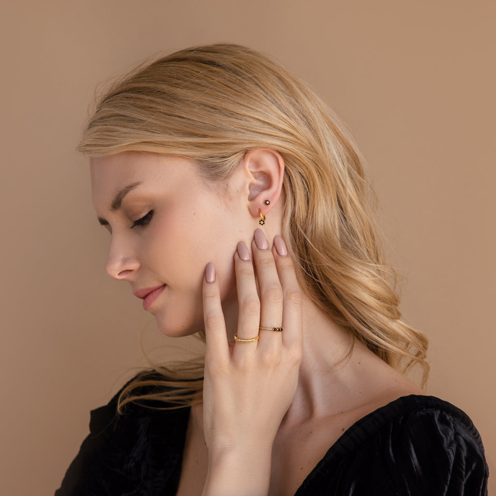 Blonde woman in profile, eyes closed, touches her neck while wearing Onyx Flower Studs and gold jewelry with a black top.