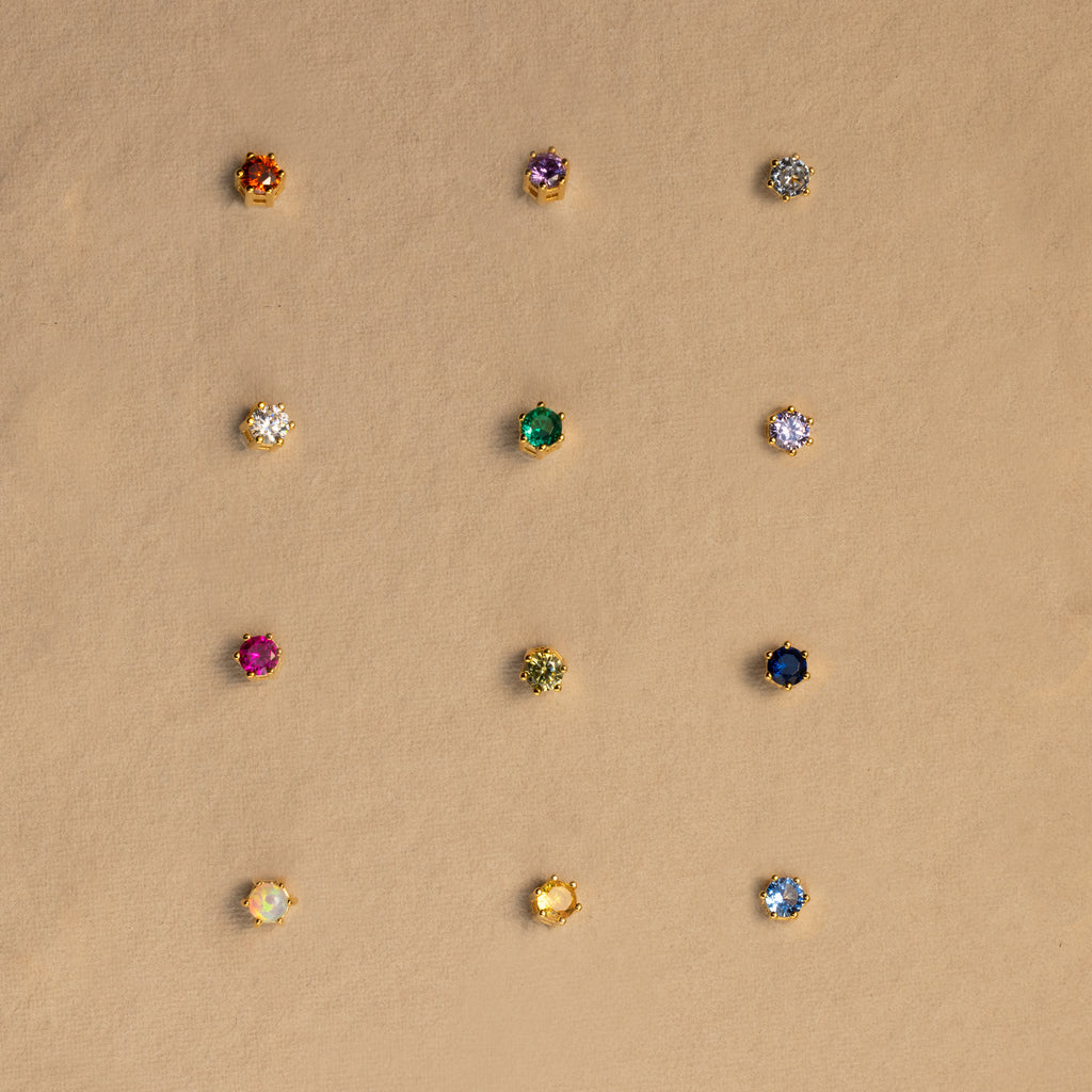 Twelve Birthstone Flatback Studs are arranged in a neat grid on a beige background, showcasing vibrant earrings in every birthstone hue.