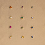 Twelve Birthstone Flatback Studs are arranged in a neat grid on a beige background, showcasing vibrant earrings in every birthstone hue.