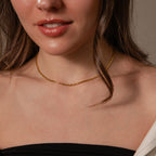 A woman with wavy brown hair wears an off-the-shoulder black top and the Bold Link Chain Necklace in 18K Gold.