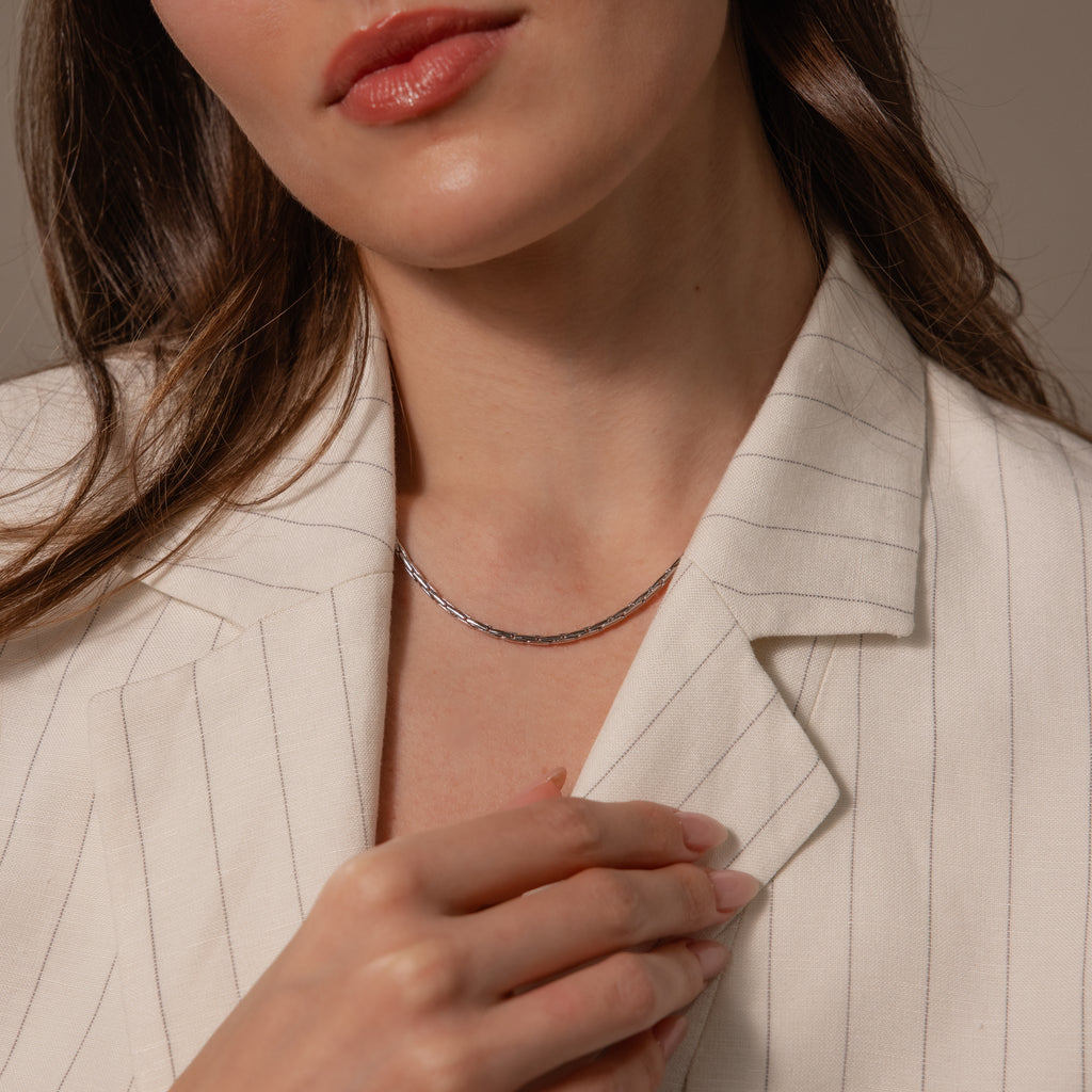 A woman wearing a cream pinstripe blazer pairs her look with the Bold Link Chain Necklace in Silver, holding her lapel with one hand.